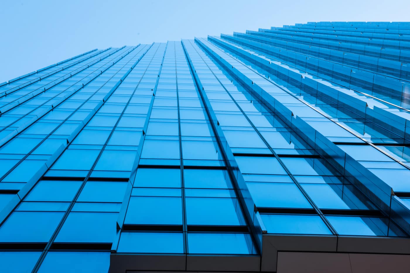 Looking up the glass facade of a modern office tower against a clear blue sky